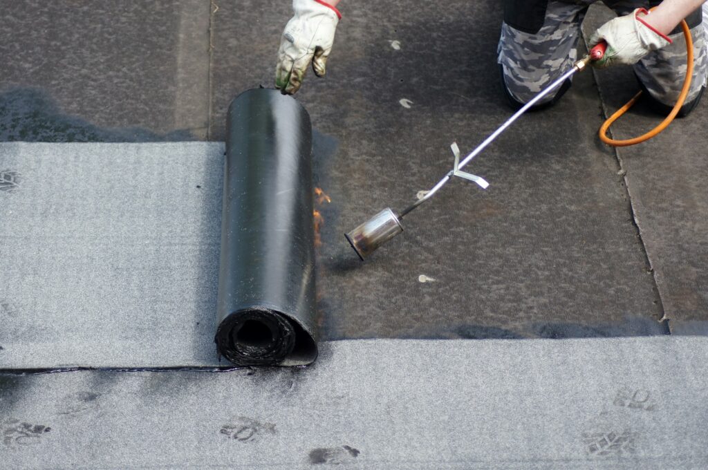 Flat roof installation with propane blowtorch during construction works with roofing felt